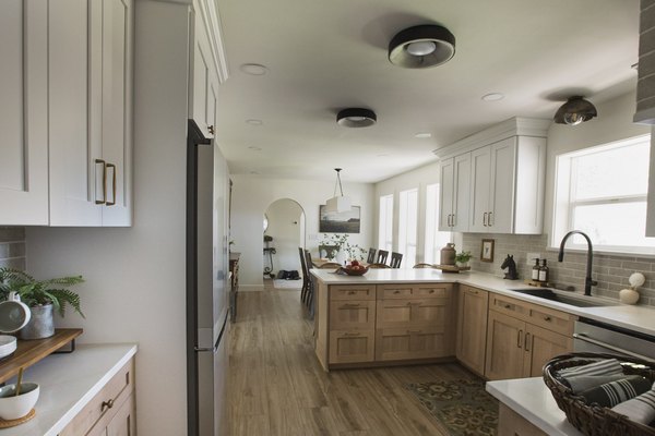 A light-wood kitchen with a white quartz peninsula, gray brick backsplash, black flush-mount lighting, and a dining table beyond
