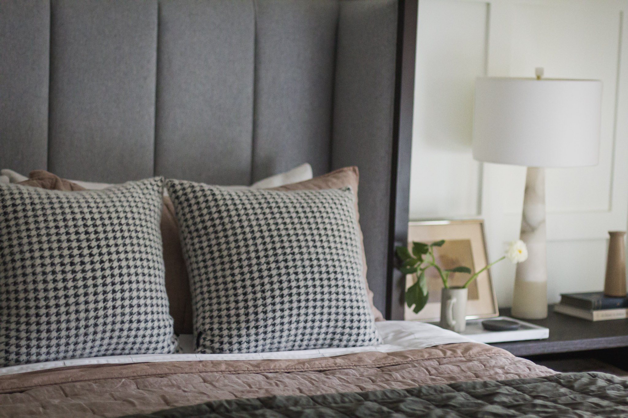 A close view of houndstooth pillows against the gray channel-tufted headboard, with the lamp-lit nightstand beyond