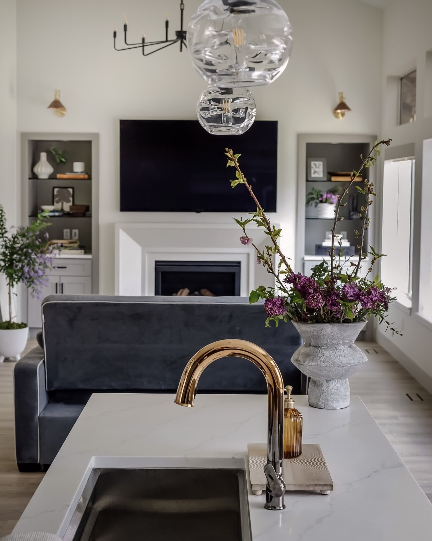 A living room seen across the kitchen island, with a navy velvet sofa, fireplace, and built-in shelving