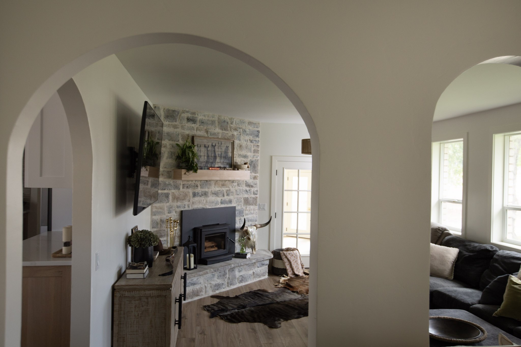 A living room seen through a plaster archway, with a stone fireplace, wood console, and a hide rug on the floor